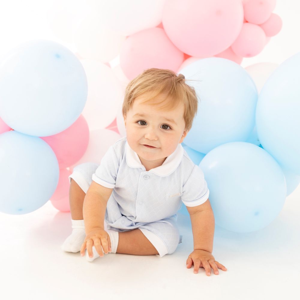 A baby boy sat on the floor amongst blue and pink balloons 