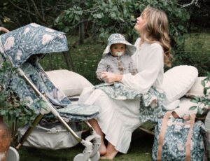 A woman sat in a garden beside a pram holding a baby