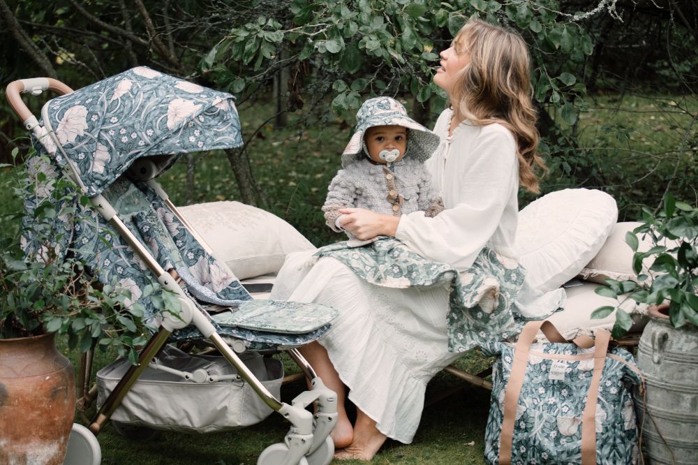 A woman sat in a garden beside a pram holding a baby