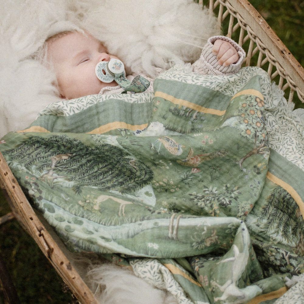 A baby lying in a crib covered in a green quilt 