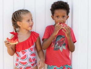 Two young children outside in summer clothing eating watermelon slices