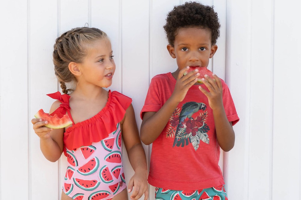 Two young children outside in summer clothing eating watermelon slices