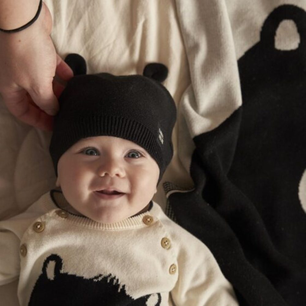 A baby wearing a black bear ear hat with a matching jumper and blanket 