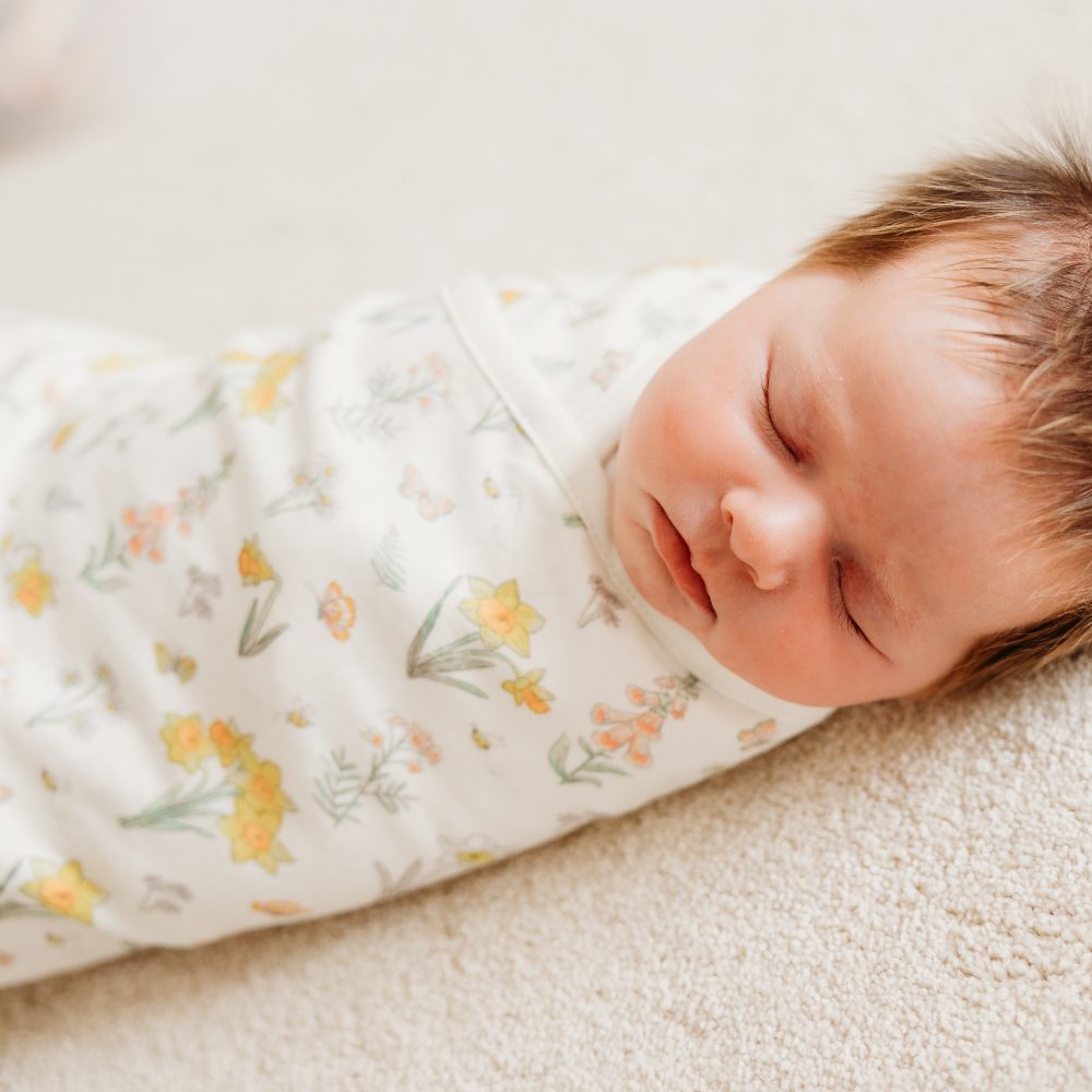 A newborn baby wrapped in a swaddle with a yellow floral print 