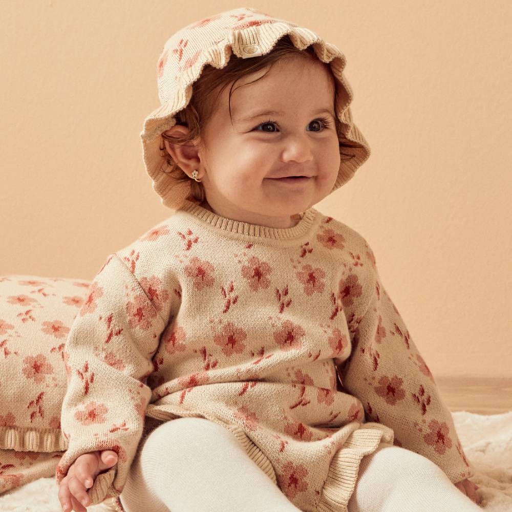 A young baby in a flowery knitted hat and dress 