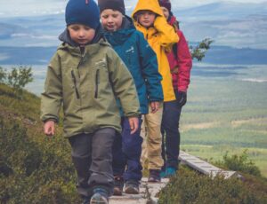 Four children walking up a hill wearing outerwear and hats by Isbjorn of Sweden