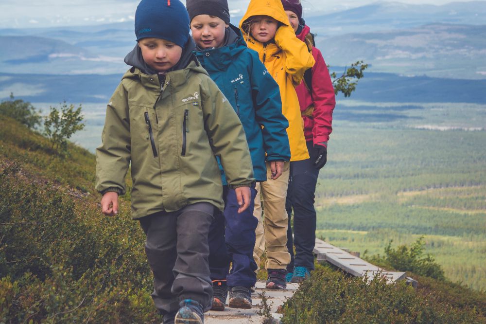 Four children walking up a hill wearing outerwear and hats by Isbjorn of Sweden