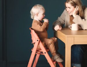 A child sat in a KAOS highchair at a table beside a woman
