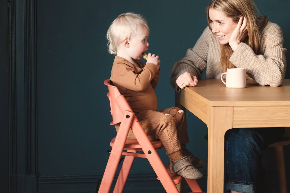 A child sat in a KAOS highchair at a table beside a woman