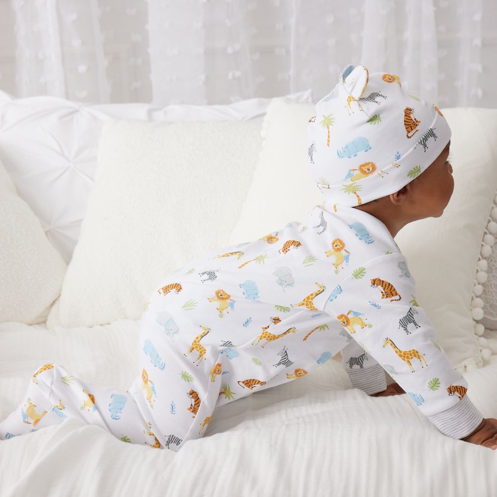 A young baby in a romper and hat crawling across a bed 