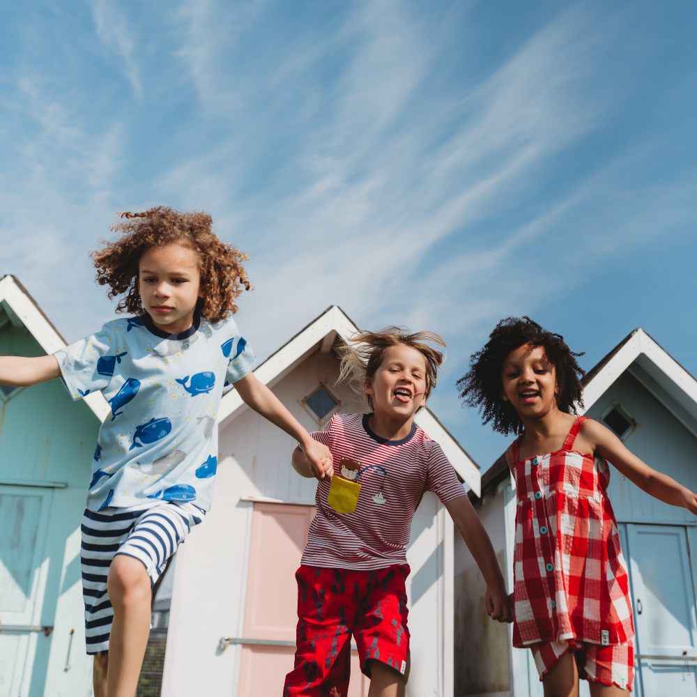 Three children outside running and holding hands in front of colourful beach huts