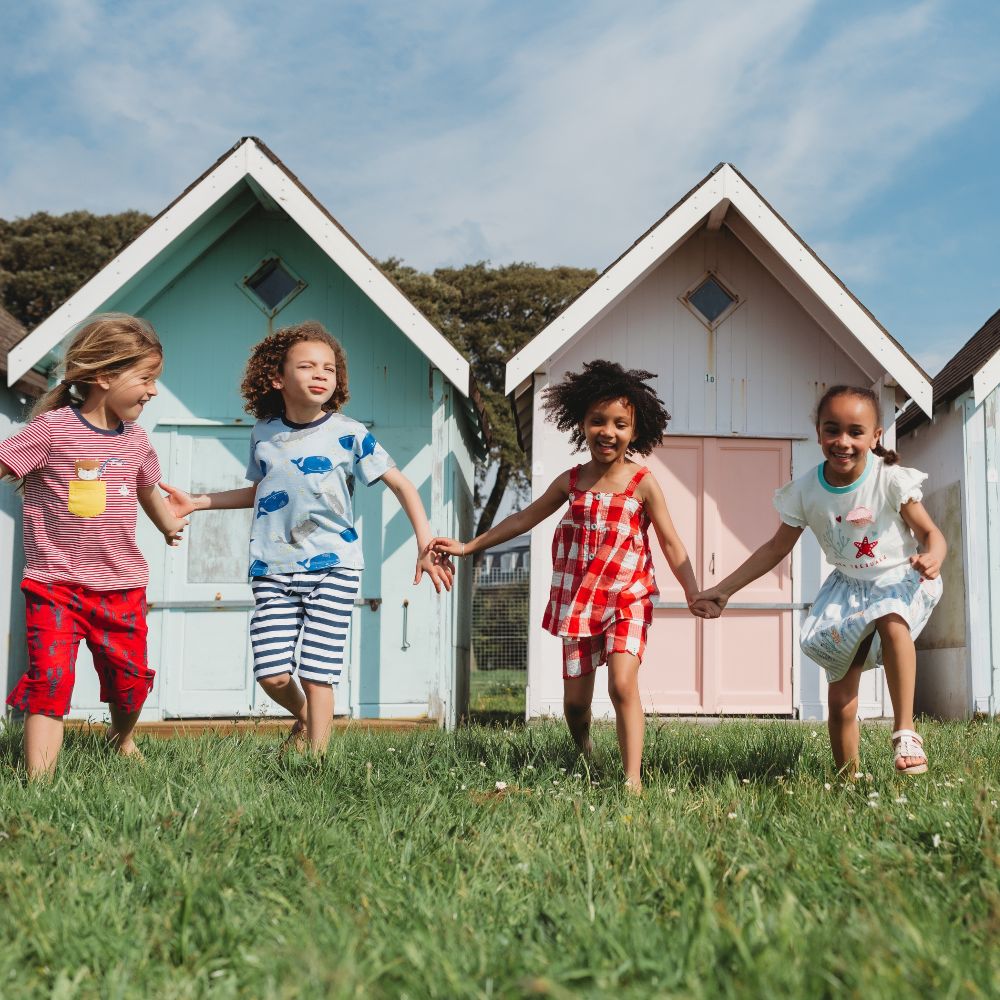 Four children running holding hands in front of beach huts 