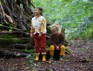 Two children in a wood wearing Fairtrade natural rubber waterproof boots by Little Green Radicals