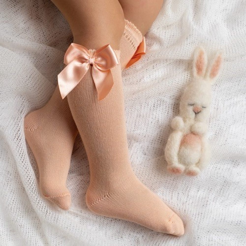A child's legs wearing peach coloured knee socks with satin bows at the top 