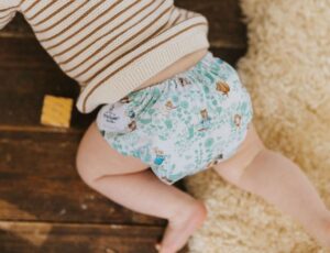 A baby crawling on a wooden floor wearing a striped jumper and a Peter Rabbit print cloth nappy by The Nappy Den