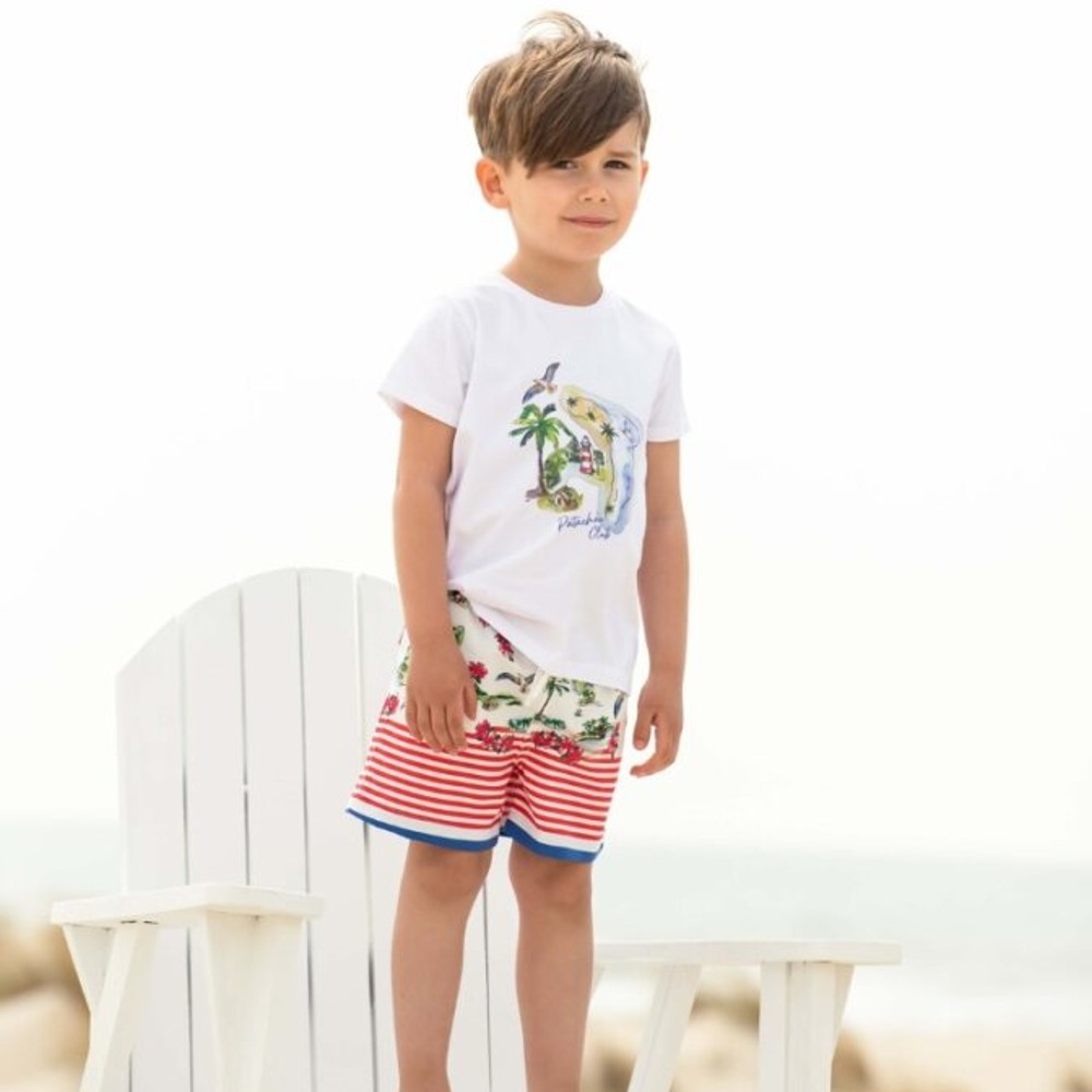A young boy outside stood on a white wooden chair wearing a T-shirt and shorts 