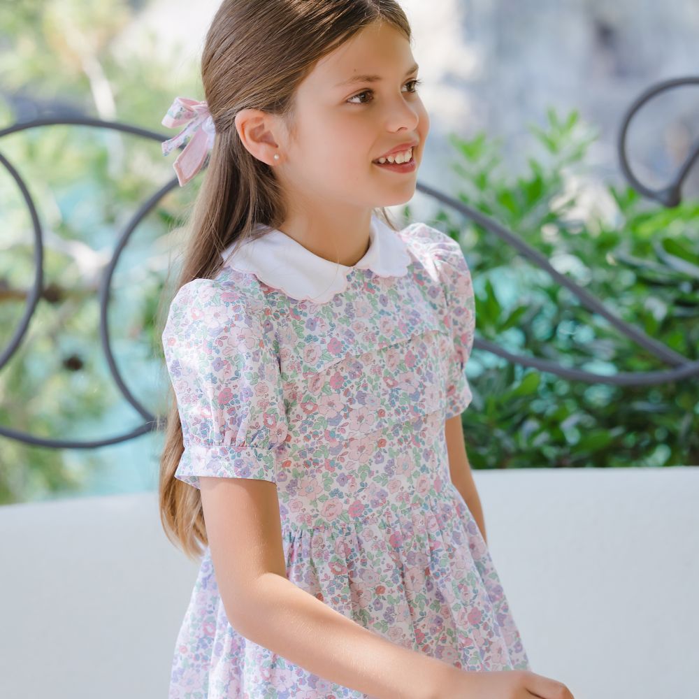 A young girl outside wearing a traditional floral dress with a white collar 