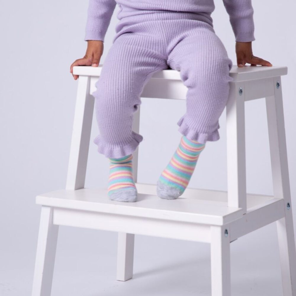 A child in a lilac coloured top and trousers and striped socks sat on a white stool 