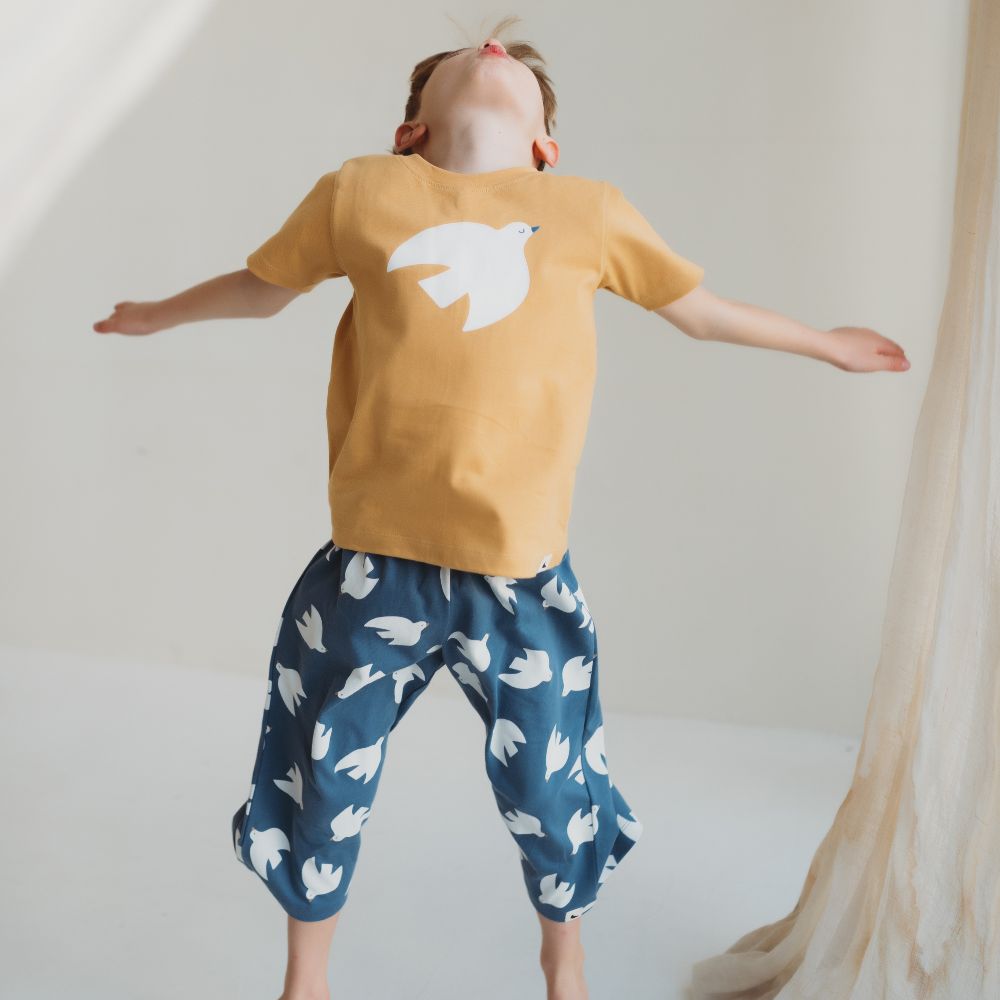 A young boy jumping in the air wearing a yellow T-shirt and blue trousers with doves on them