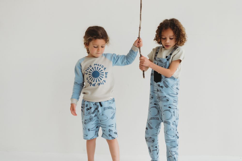 Two young children holding a large stick wearing outfits from the Free as a Bird collection by Turtledove London