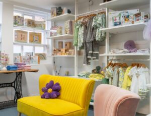 The interior of lifestyle store Bloom & Alfie displaying children's clothes and accessories and a yellow sofa with a purple flower cushion