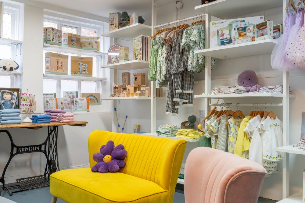 The interior of lifestyle store Bloom & Alfie displaying children's clothes and accessories and a yellow sofa with a purple flower cushion