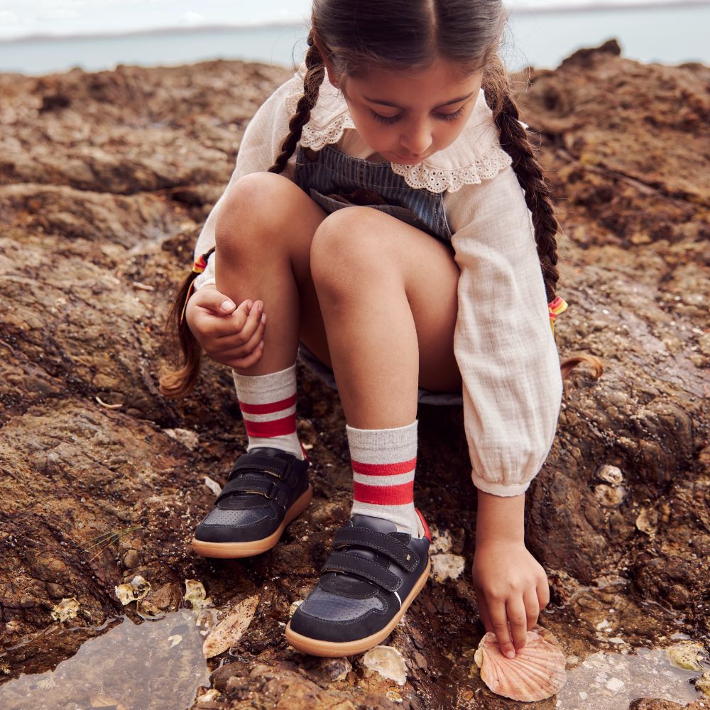 A young girl crouched beside a rock pool wearing a navy dress and shoes 