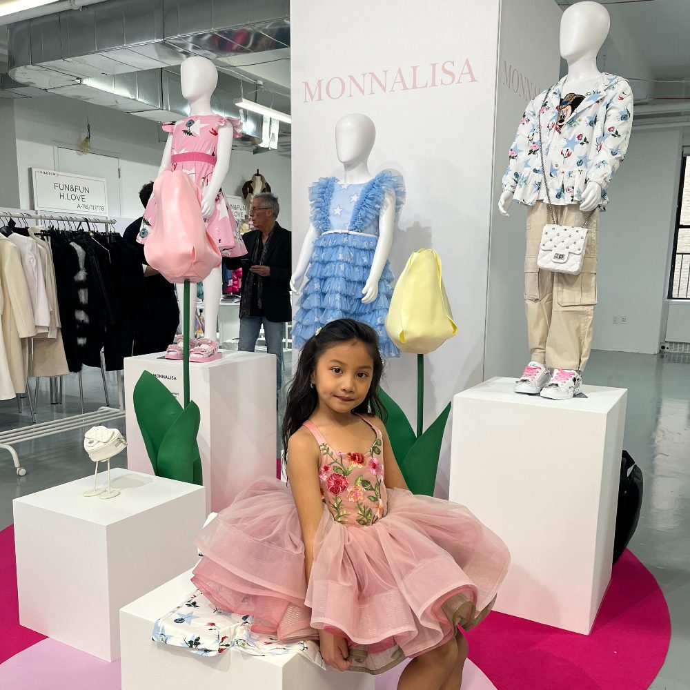 A young girl sat on a display of children's clothes on mannequins at Children's Show 