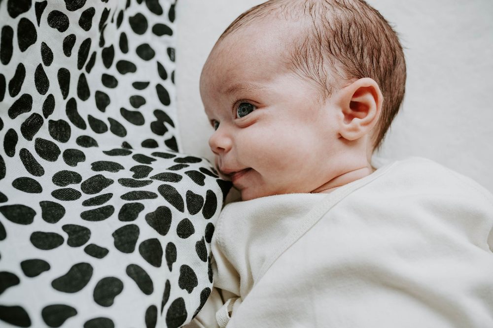 A baby lying beside a black and white spotty blanket