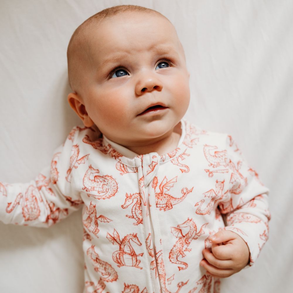 A young baby wearing a babygro with a red dragon print on it 