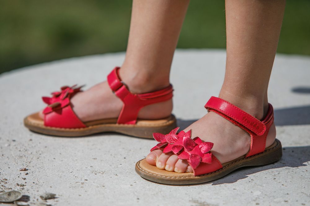 A child's feet wearing red leather sandals with flowers on the straps 