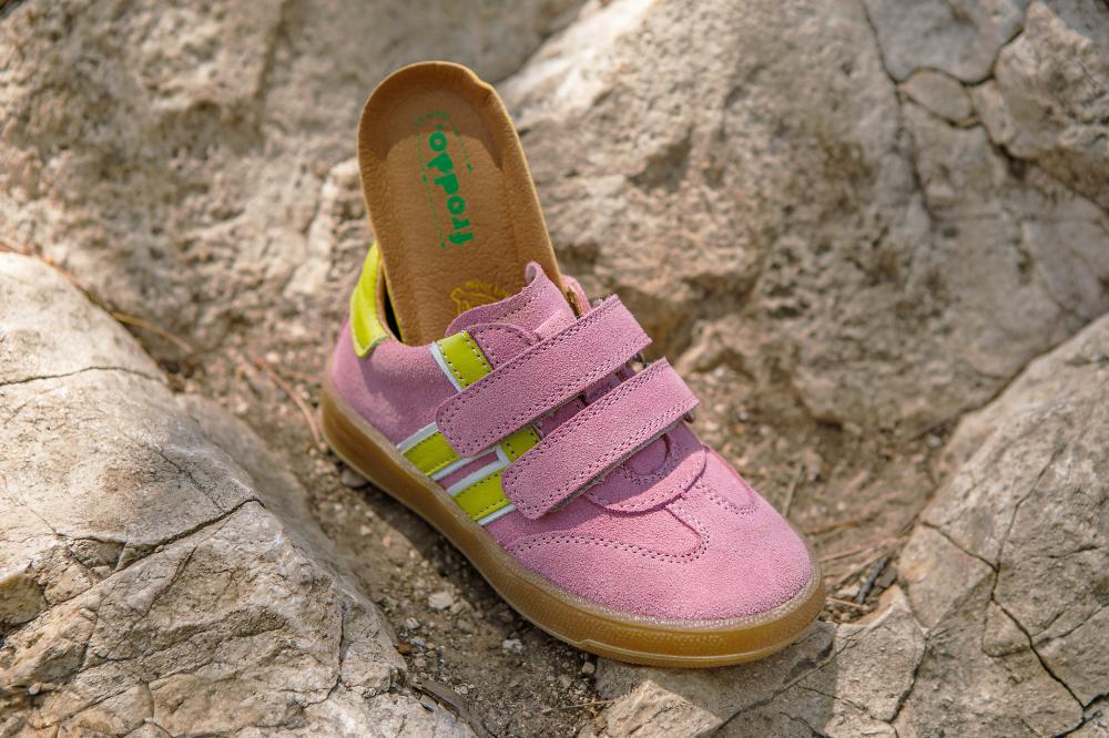 A pink Froddo trainer with yellow stripes displayed on a rock 