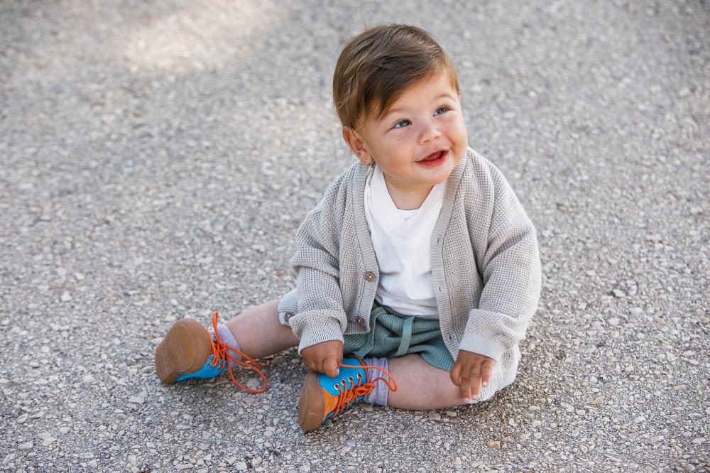 A young child sat outside on the floor wearing blue and orange lace-up shoes by Froddo 