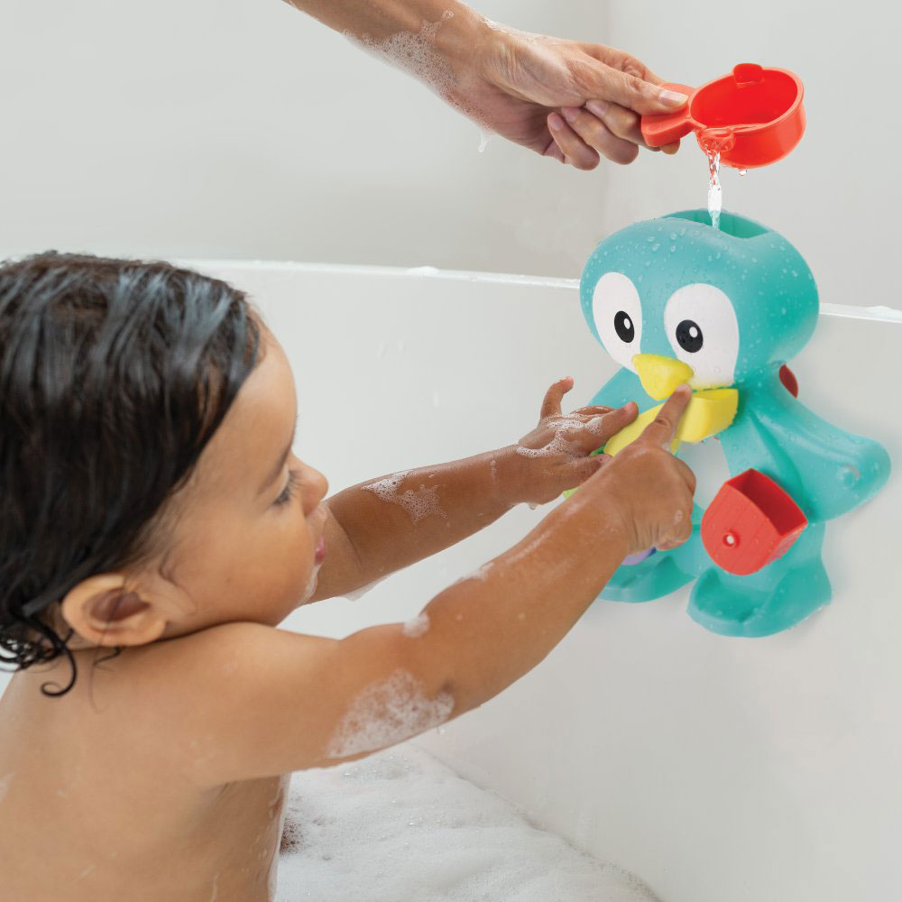 A young child sat in the bath playing with the tub-a-penguin toy