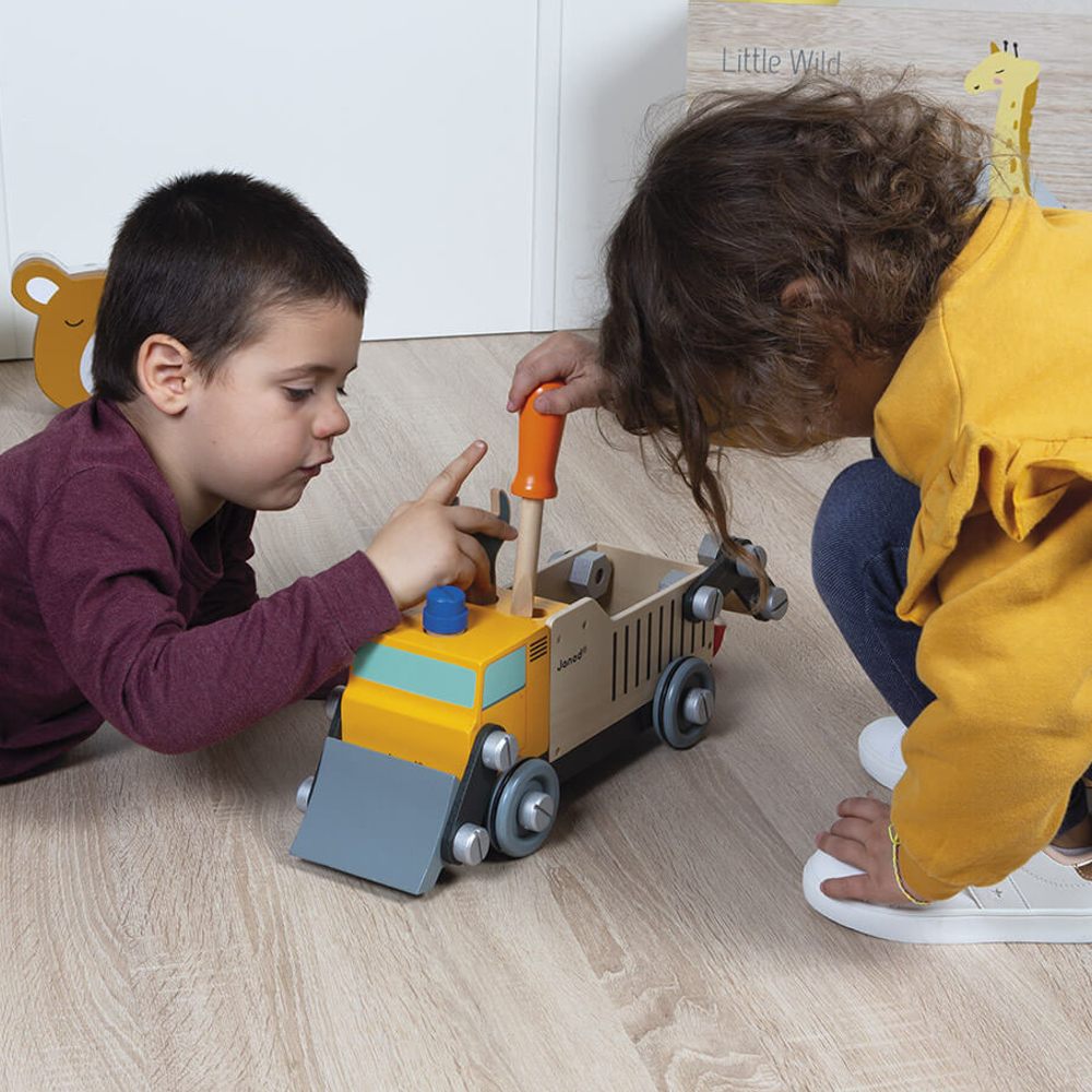 Two children sat on a floor playing with a wooden truck toy by Janod 