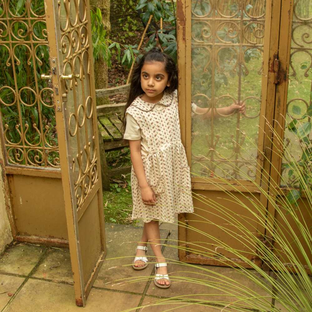 A young girl in a dress stood in the doorway of an outdoor building 