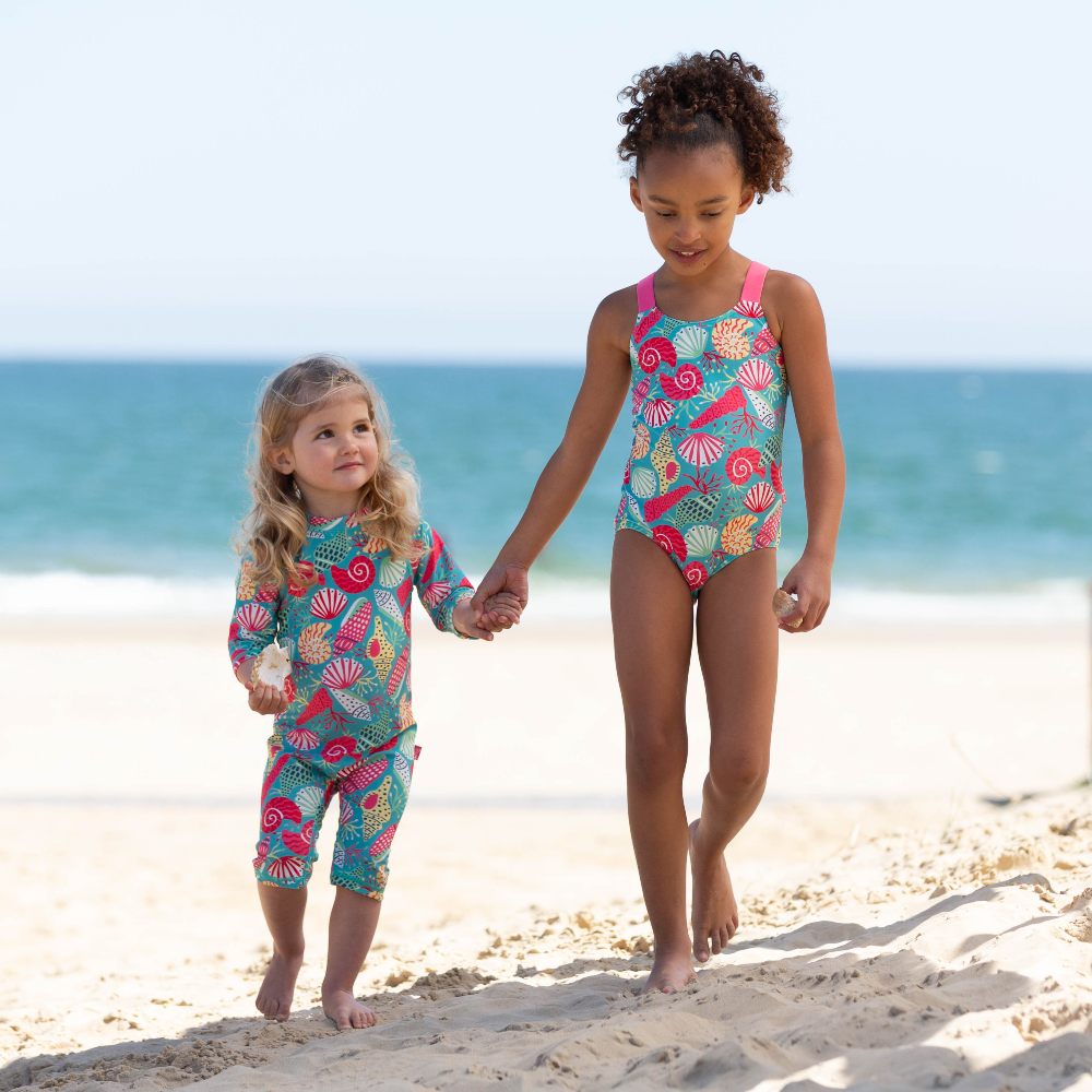 Two young girls holding hands wearing brightly coloured swimwear on a beach 