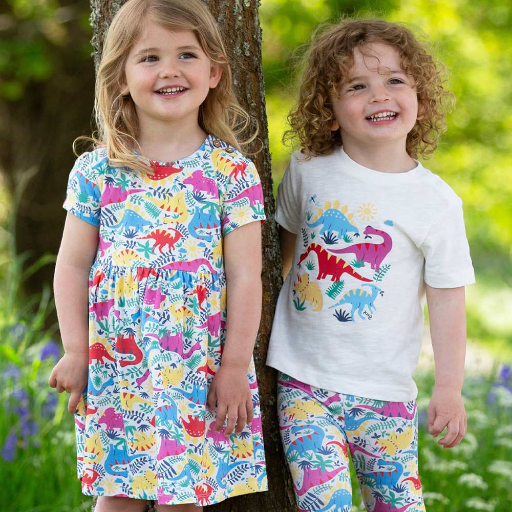 Two children stood outside in front of a tree wearing brightly coloured outfits 