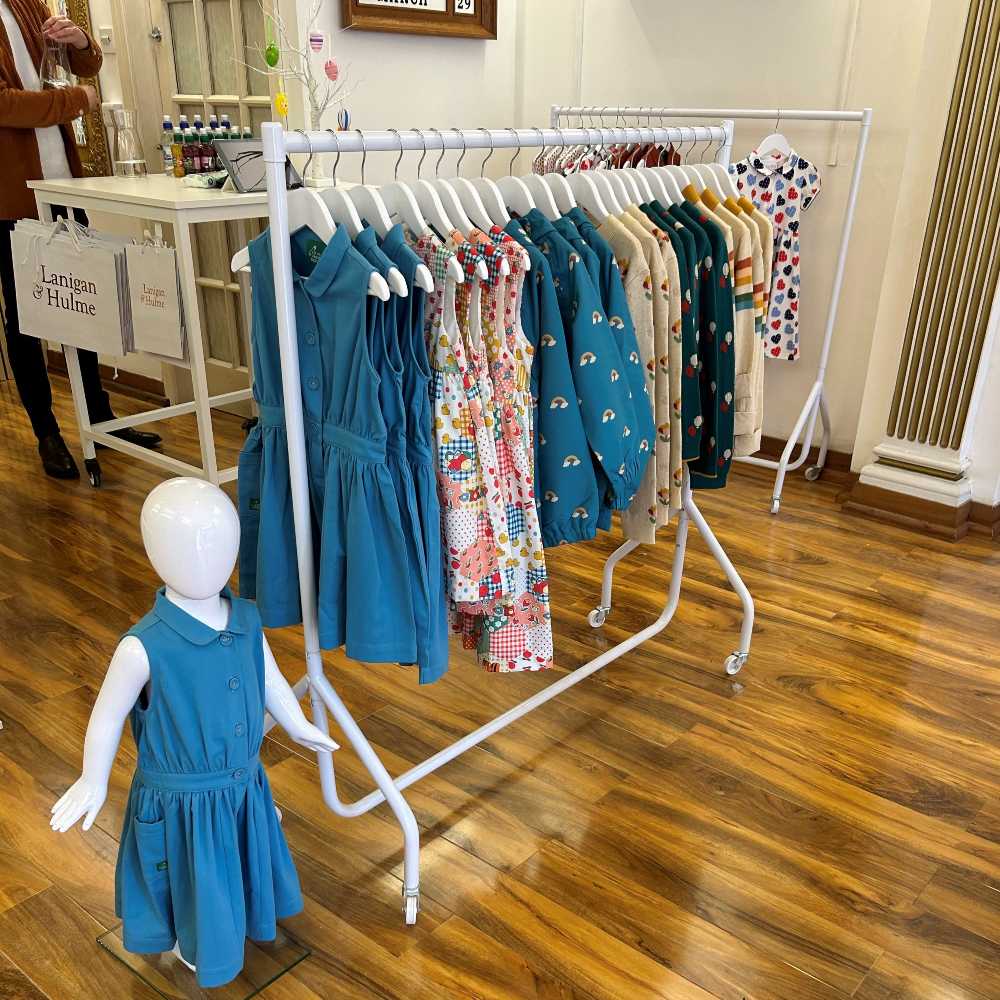 A rail of children's clothes beside a child mannequin wearing a blue dress inside a childrenswear store 