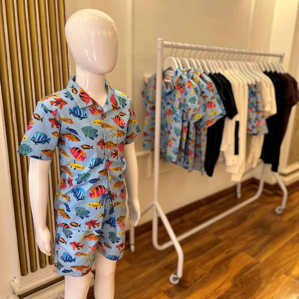 A boys shirt and shorts displayed on a mannequin beside a rail of children's clothes in a shop 