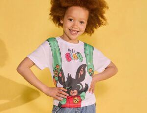 A child stood against a yellow background wearing a Matalan x NSPCC T-shirt