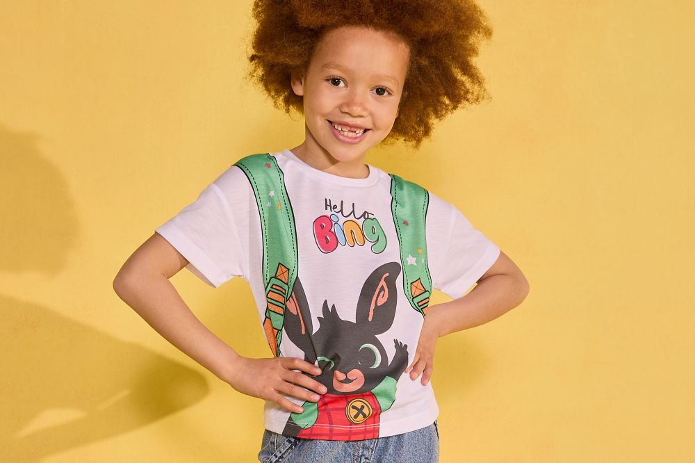 A child stood against a yellow background wearing a Matalan x NSPCC T-shirt