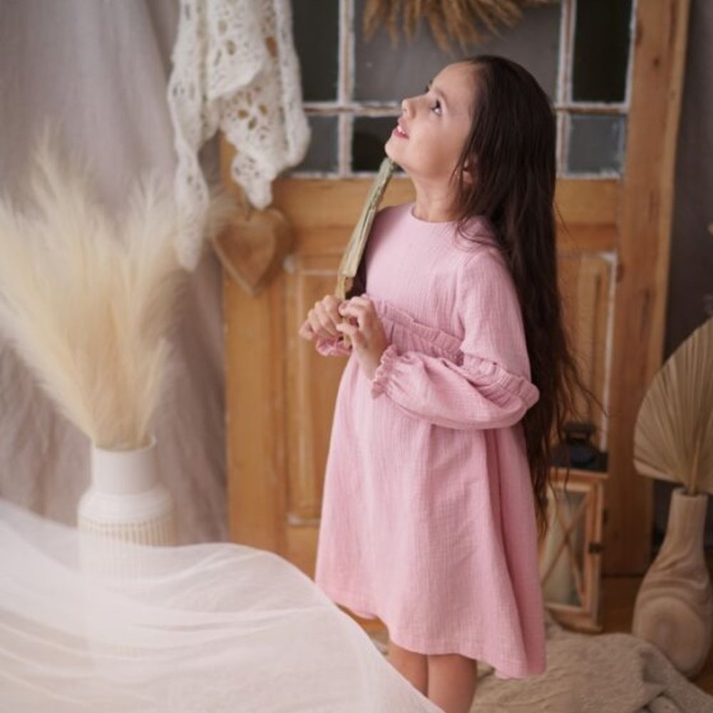 A young girl stood in a room wearing a pale pink dress 