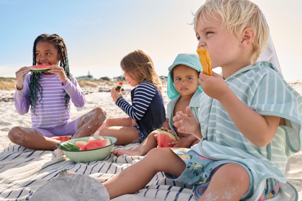 A group of children sat on a beach eating watermelon slices 