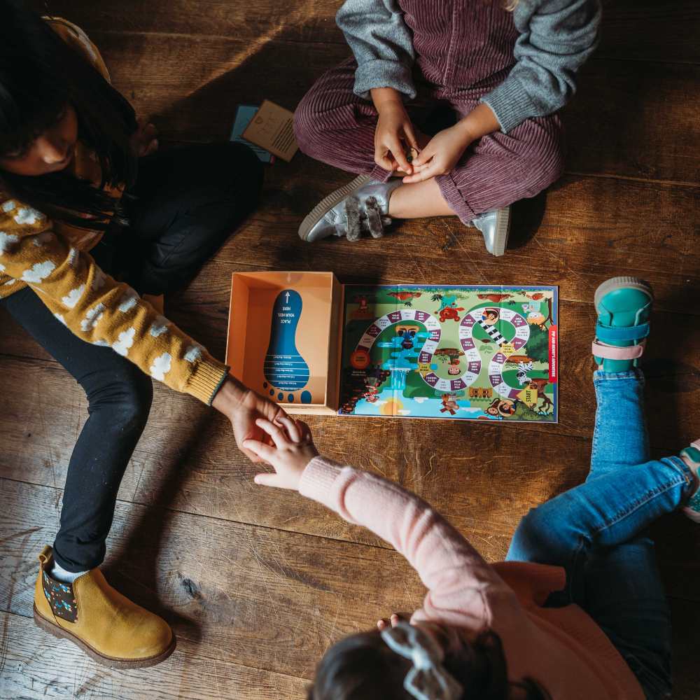 Three children sat on a wooden floor playing a board game 