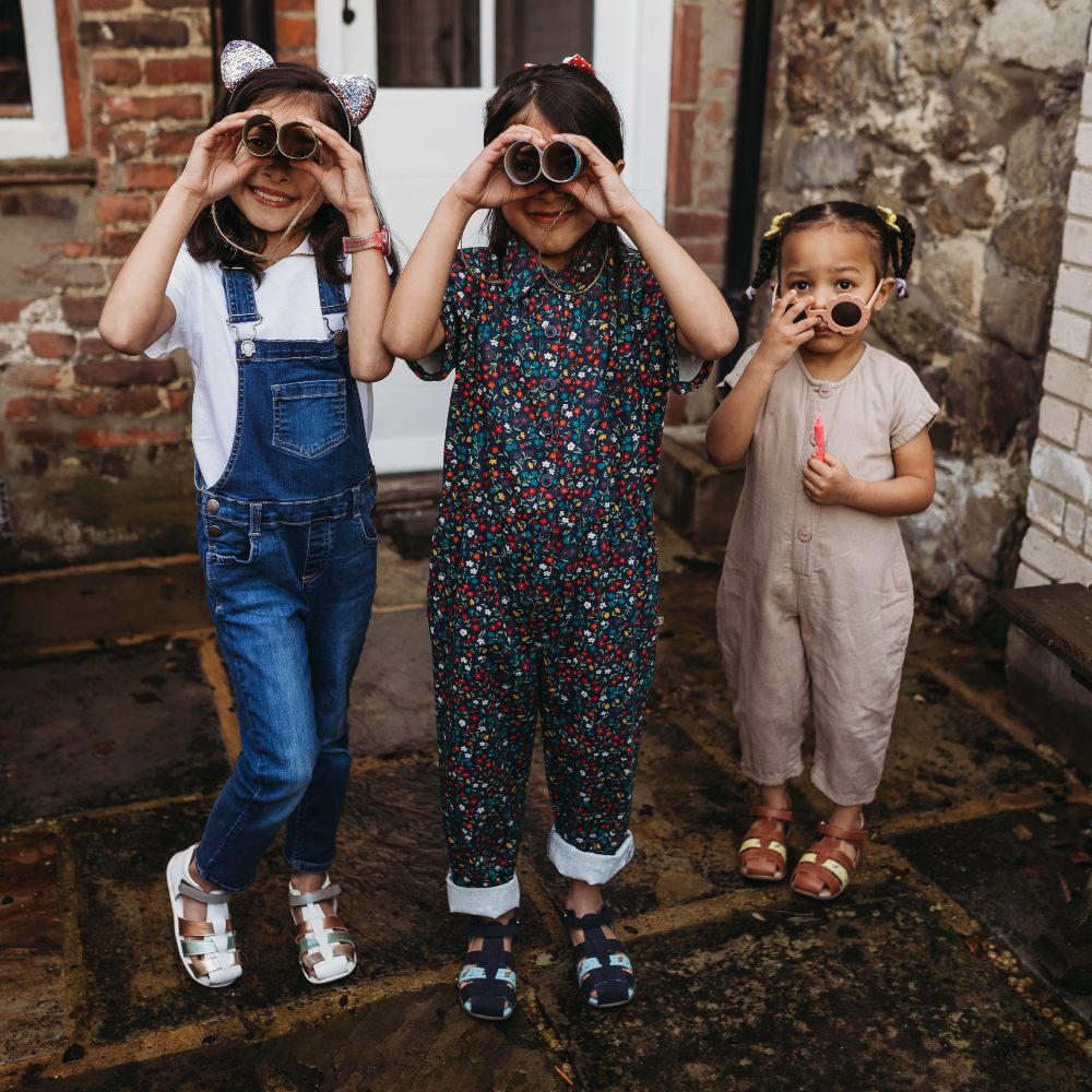 Three young girls stood at the back of the house pretending to look through binoculars 