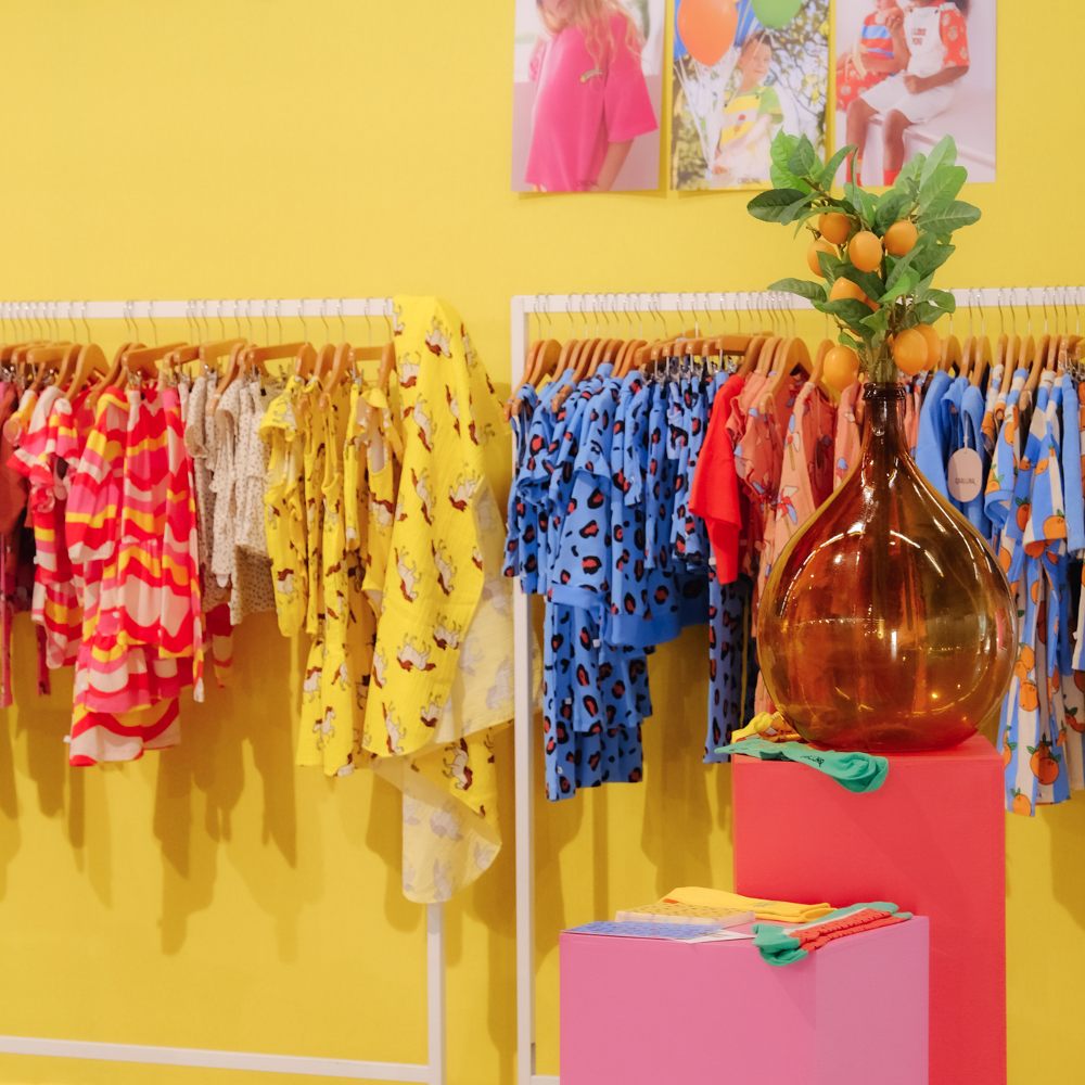 A stand at Playtime Paris with a rail displaying children's clothes against a yellow wall with pink display stands