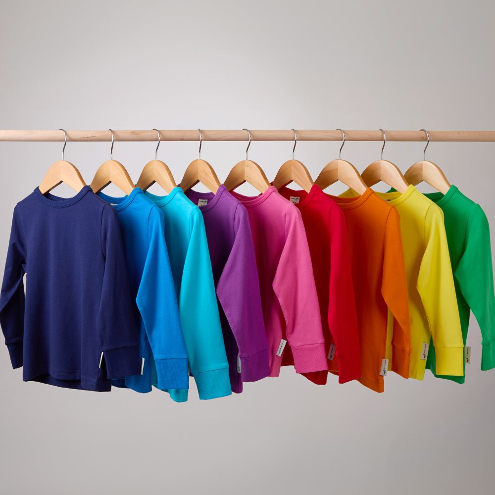 Different brightly coloured children's tops hung on a wooden rail 