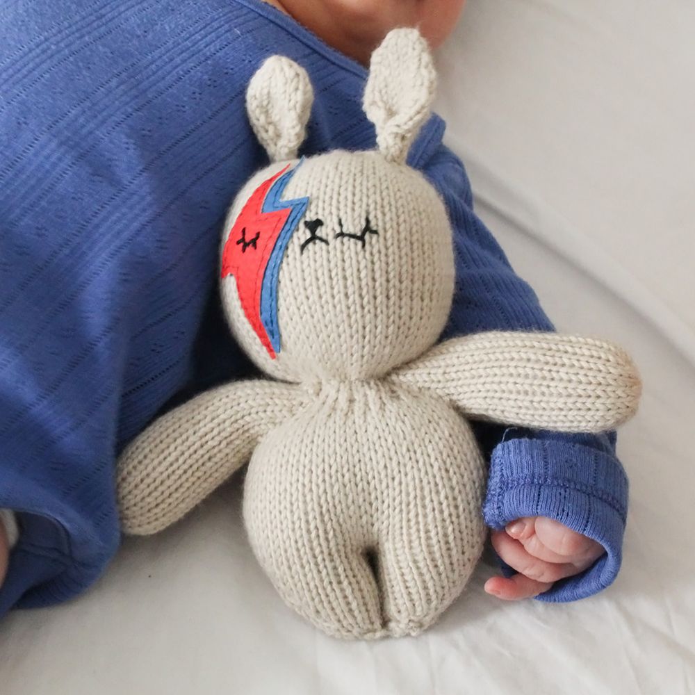 A knitted rabbit toy beside a baby in a blue babygro 