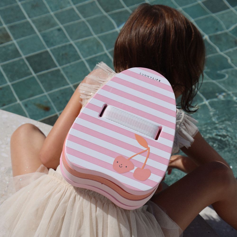 A child leaning into a pool wearing a pink a pink tutu skirt and a striped float on her back